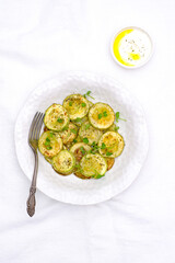 Fried zucchini with lemon zest and thyme, cream sauce on white background. Top view.