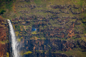 Waipo’o Falls at Waimea Canyon getting a close look from a helicopter.  Waip’o Falls, a glorious two-tier, 800 foot waterfall, cascades into the deep and colorful gorge of the Waimea Canyon below.  - 765133470