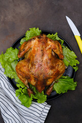 Chicken grill on lettuce on leaves on black plate with yellow knife, napkin isolated on dark background.