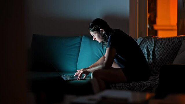 Nighttime Computing - Woman On Sofa With Laptop And Headphones In Dimly Lit Room. Woman Browsing Internet In The Evening, In Front Of Computer Screen