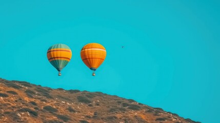 Obraz premium a couple of hot air balloons flying in the sky over a mountain side with a bird flying in the distance.