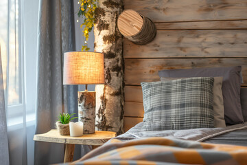 Cozy Bedroom Corner with Rustic Wooden Accent Wall and Warm Lighting. Rustic Charm. Bedside Table with Lamp and Plaid Pillows in Wooden Cabin Bedroom