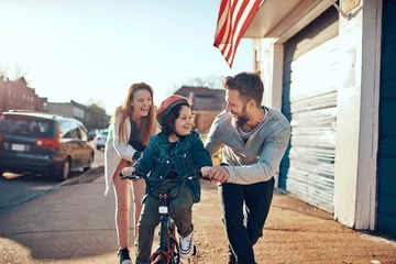 Foto op Canvas Happy family teaching child to ride a bicycle outdoors © Geber86