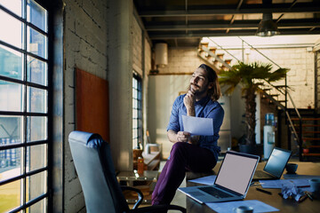 Obraz na płótnie Canvas Businessman with documents sitting on desk with laptops in modern loft office