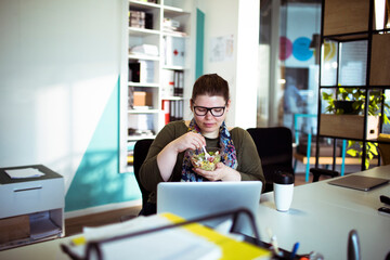 Smiling woman eating salad at her desk in office