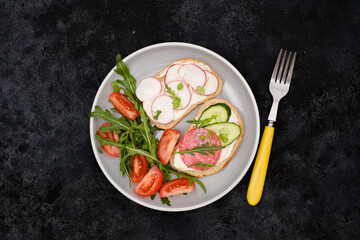 Different tapsas sandwiches with vegetables, radish, sausage, tomatoes, arugula on grey plate on dark background. top view.