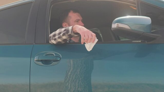 A man sits in a car and throws trash out the window.
