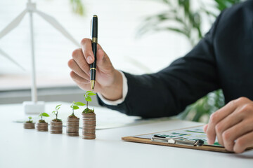 Businessman with coin stack at his office as sustainable money growth investment or eco-subsidize. Green corporate promot and invest in environmental awareness. Gyre