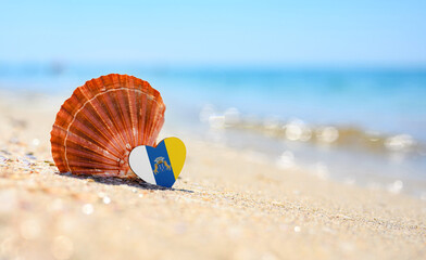 Sandy beach in the Canary Islands. Flag of the Canary Islands in the shape of a heart and a large shell. A wonderful seaside resort.