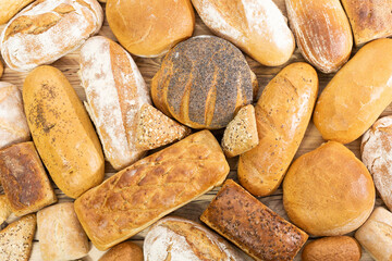 Many kinds of bread and buns randomly placed next to each other on a wooden countertop as decoration of a traditional bakery with a multi-generational experience. View from above.