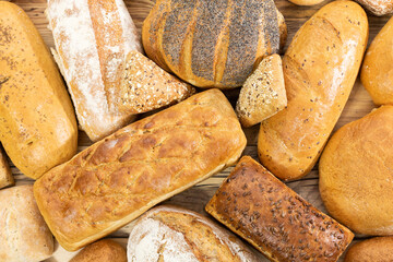 Many kinds of bread and buns randomly placed next to each other on a wooden countertop as decoration of a traditional bakery with a multi-generational experience. View from above.