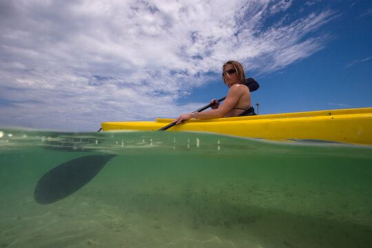 Over and under picture of woman in kayak in clear ocean water.