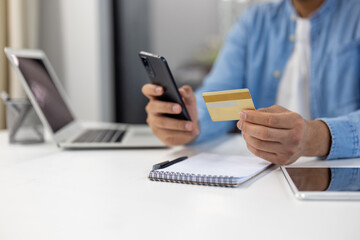 Fototapeta premium A man is using his cell phone and laptop to pay for something
