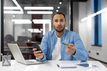 A man is sitting at a desk with a laptop and a cell phone