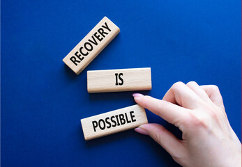 Recovery is possible symbol. Concept words Recovery is possible on wooden blocks. Beautiful deep blue background. Businessman hand. Business and Recovery is possible concept. Copy space.