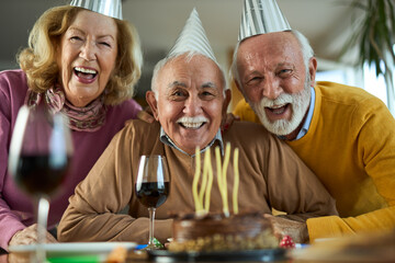 Group of senior friends having fun while celebrating Birthday at home. They are looking at camera