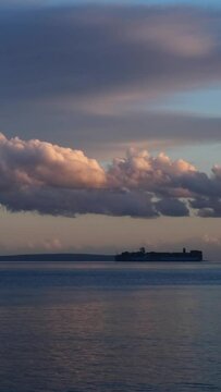 Fast motion of fluffy clouds moving in straight line above an anchored cargo ship. Sunset time by the Mediterranean sea near Krk Island, Croatia. Magnificent nature, last colourful rays of the sun.