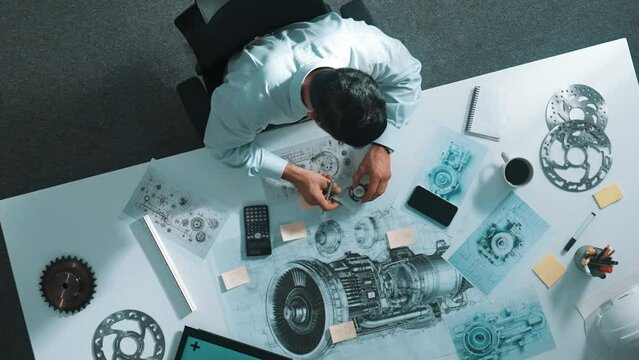 Top down view of skilled engineer writing and planning turbine engine design while sitting at meeting table with gear and electronic generator scatter around. Technician taking a note. Alimentation.