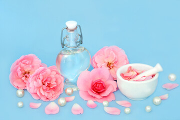 Rose flower perfume in heart shaped bottle with pearls, flowers and pink petals on blue. Natural fragrant floral  product, gift for Valentines Day, birthday, anniversary or Mothers day. - 765232854