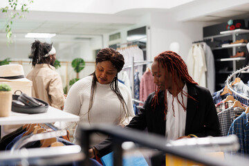 African american women friends browsing apparel and accessories in clothing store. Girlfriends...
