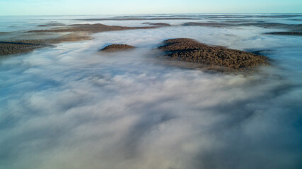 Aerial view above the clouds over forest and lakes at sunrise