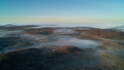 Aerial view above the clouds over forest and lakes at sunrise