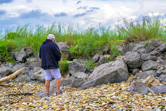 My wife is walking along this colorful stone beach at a park in Upstate NY along the shores of Lake Ontario. A woman in shorts and a sweatshirt admires the stones and boulders around her.