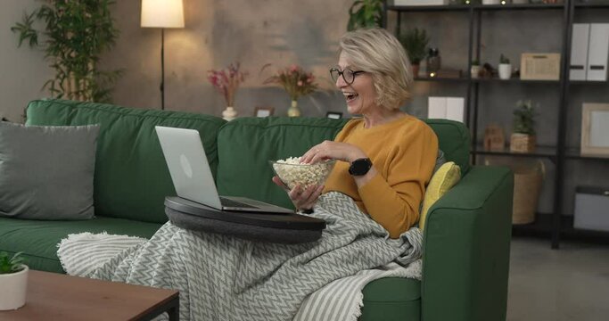 one mature blonde woman sit at home with watch movie video on laptop