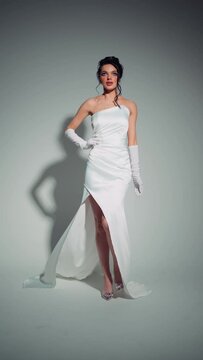 Graceful woman adorned with rhinestones, wearing satin white gown with long gloves, posing with air of elegance. Sophisticated Woman in Elegant White Gown with Rhinestone Accents.