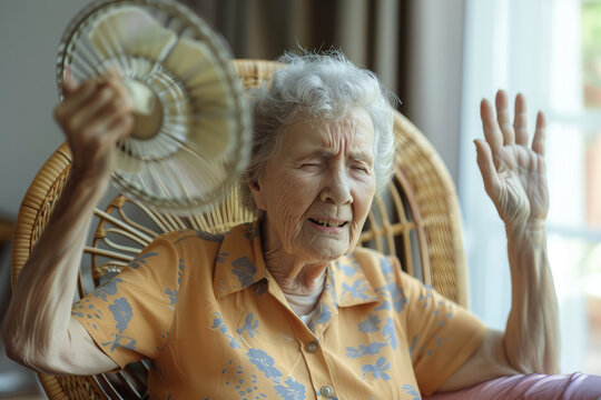 Stressed old woman waving fan suffer from overheating at home