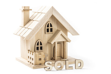 Wooden letters spelling SOLD in front of a wooden model of an elegant house suggesting a real estate transaction isolated on white