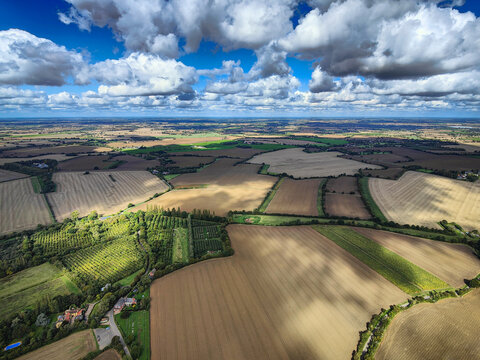 Aerial view of a typical British countryside patchwork. Agriculture fields, farm rural landscape, blue sky and white clouds. Suffolk, England, UK