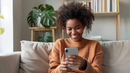 A woman is sitting on a couch and smiling while looking at her cell phone - 765272480