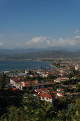 Fototapeta na wymiar A view of the city Fethiye in Turkey, a clear blue sky, the sea and mountains, a large marina on one side, buildings have red roofs, and greenery around the town