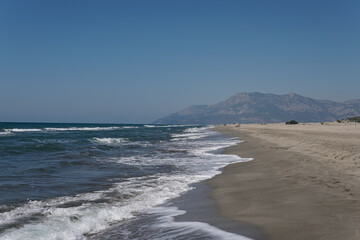 Beach with white sand and blue clear water, mountains in the background, bright blue sky, sunny day