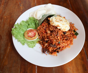 Nasi Goreng - Indonesian Fried Rice on white plate on wooden table. Nasi Goreng is an Indonesian cuisine dish with jasmine rice, chicken meat, onion, egg, vegetables. Indonesian Food. 