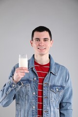 Happy man with milk mustache holding glass of tasty dairy drink on gray background