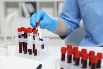 Laboratory testing. Doctor with blood samples in tubes at white table indoors, closeup