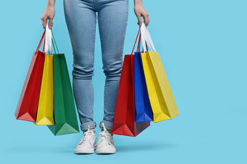 Woman with shopping bags on light blue background, closeup. Space for text