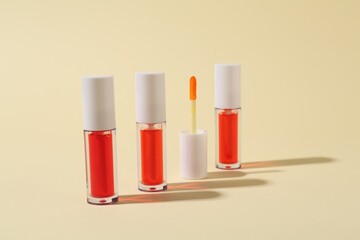 Bright lip glosses and applicator on beige background