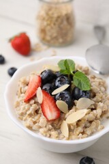Tasty oatmeal with strawberries, blueberries and almond petals in bowl on white wooden table
