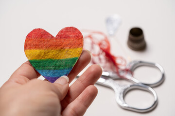 mano sosteniendo corazón pintado como bandera de orgullo gay con herramientas en el fondo 