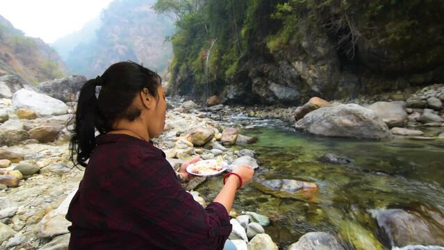 A female traveler enjoying Momo on the bank of a mountain river.