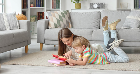 Little boy and his mother reading book while lying on floor at home