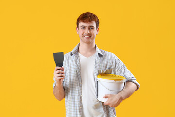 Young man with putty knife and bucket on yellow background