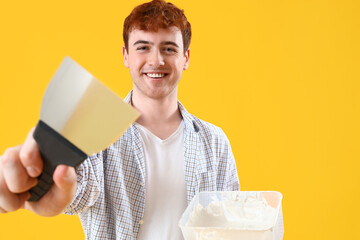 Young man with putty knife and plaster on yellow background