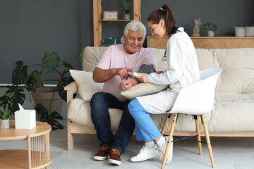 Obraz premium Young nurse measuring blood pressure of senior man at home