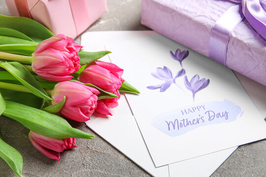 Envelope with festive postcard, gift boxes and tulips on grey grunge background. Happy Mother's Day