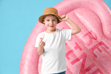 Cute little boy with swim mattress making heart gesture on blue background