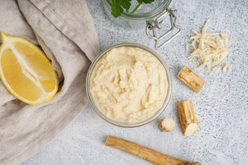 Horseradish sauce in glass bowl with lemon and horseradish roots on white background